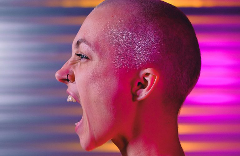 young woman with a shaved head and a nose earring screaming